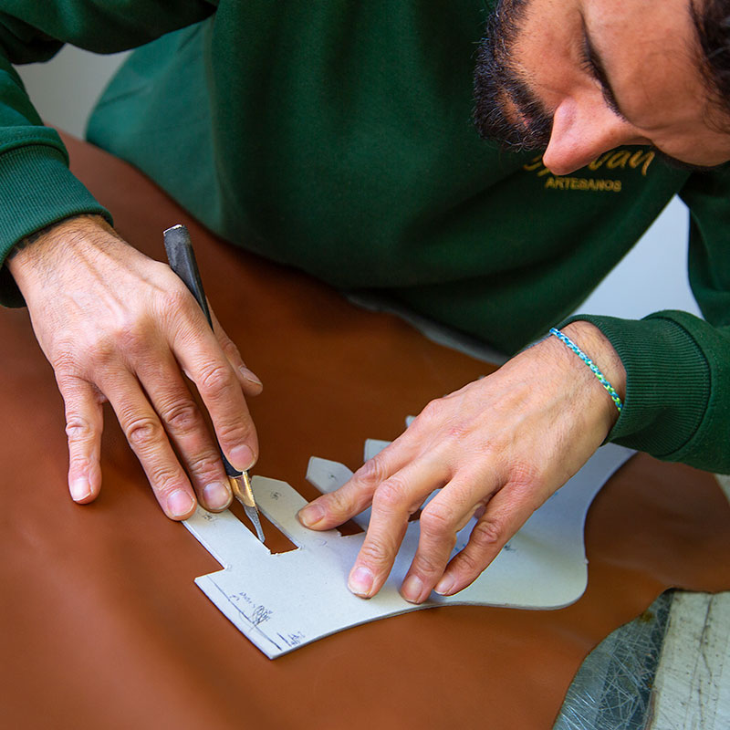 Hombre cortando una pieza de piel con un patrón y una cuchilla