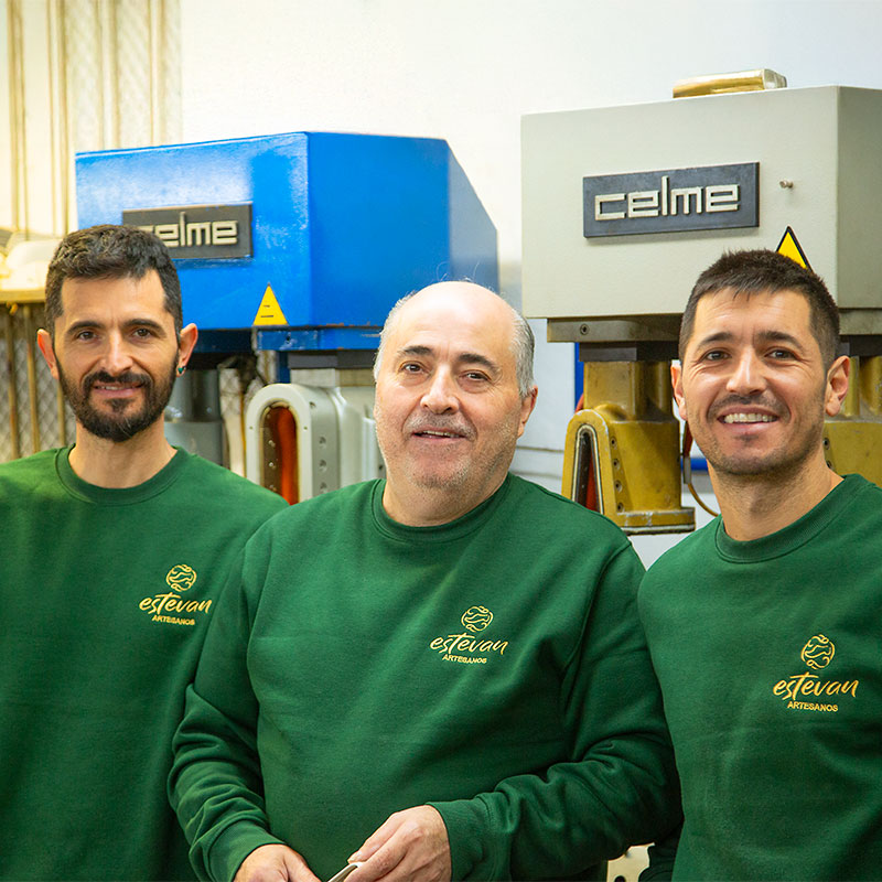 Tres hombres sonriendo delante de maquinaria de fabricación de calzado